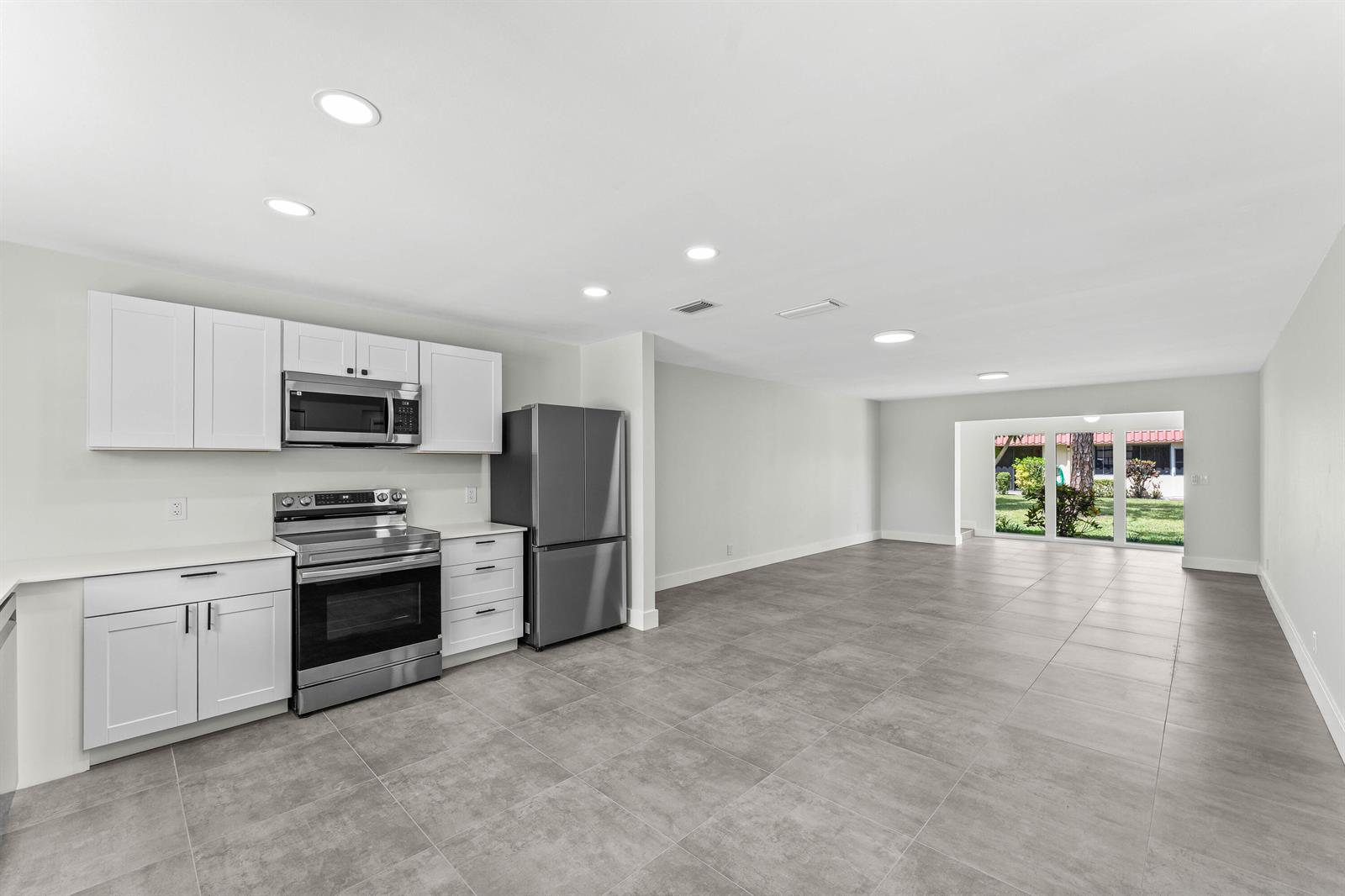 A modern kitchen with white cabinets and stainless steel appliances opens to a tiled living area — 711 Laconia Circle # B, FL 33467, FL