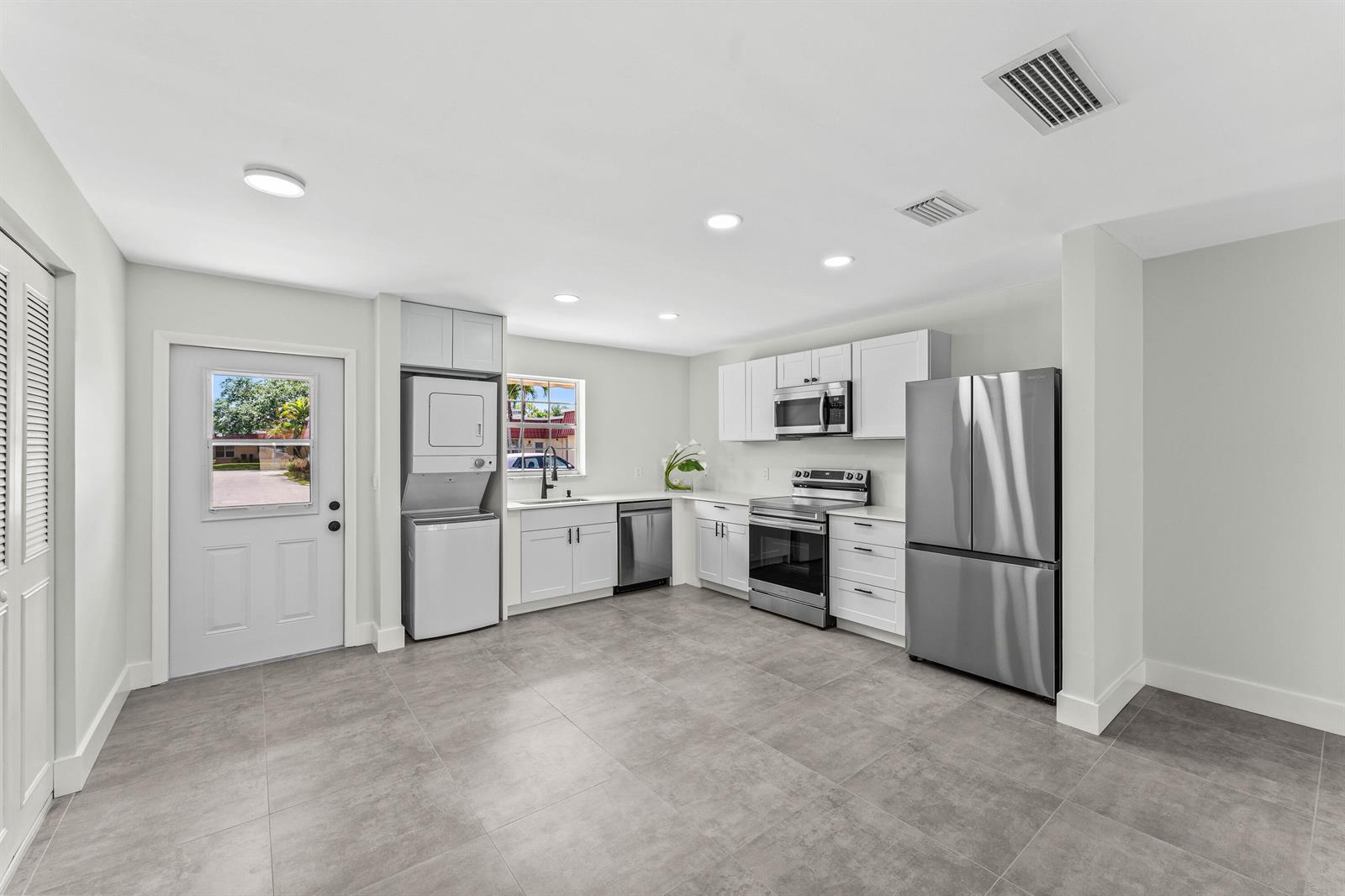A modern kitchen features white cabinetry, stainless steel appliances, and gray tile flooring — 711 Laconia Circle # B, FL 33467, FL