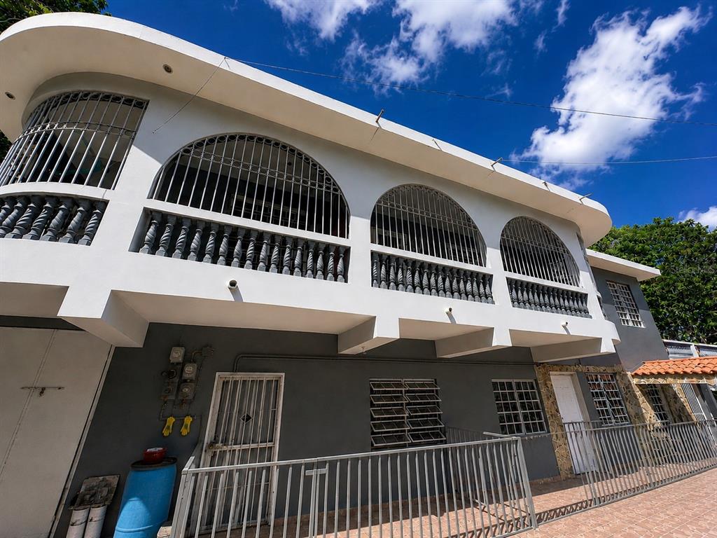 A two-story building with a white arched balcony, metal security bars, and a gray ground floor — Carretera 132 BO. TALLABOA ALTA, PENUELAS, PR