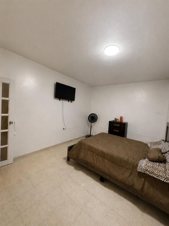 A bedroom features white walls, tile flooring, a bed with brown bedding, and a wall-mounted television — Carretera 132 BO. TALLABOA ALTA, PENUELAS, PR