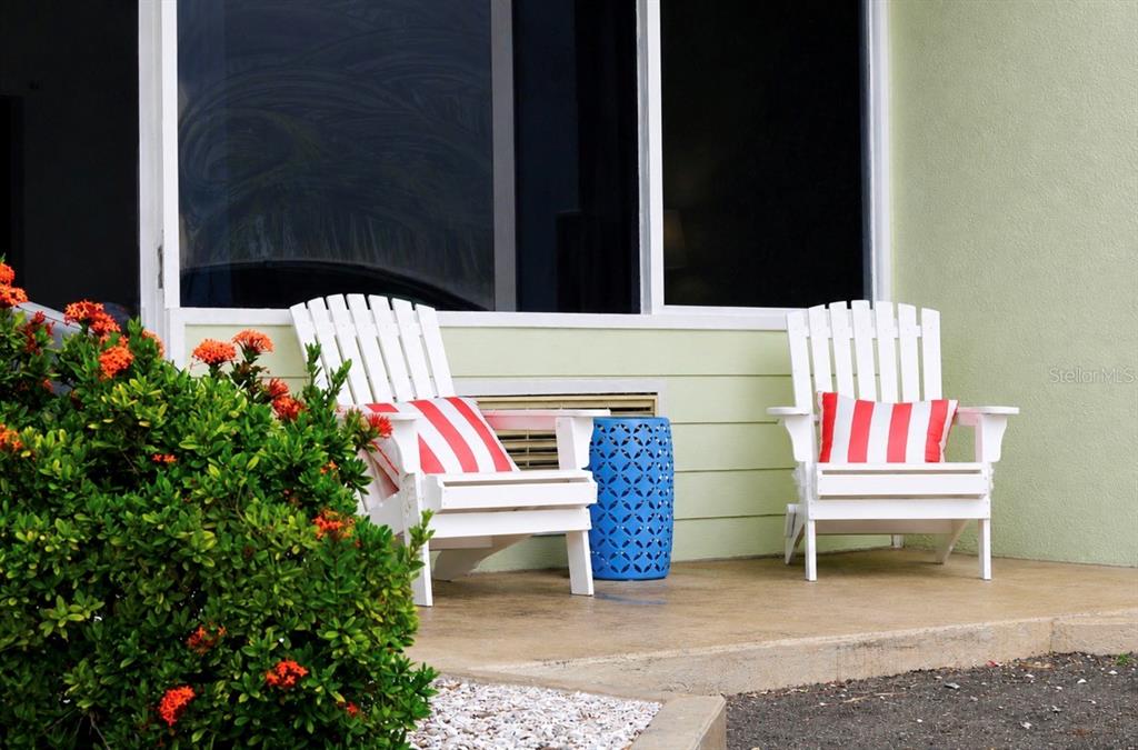 Two white Adirondack chairs with red striped pillows sit on a patio near a bush — 611 DESTINY DRIVE UNIT 307, RUSKIN, FL