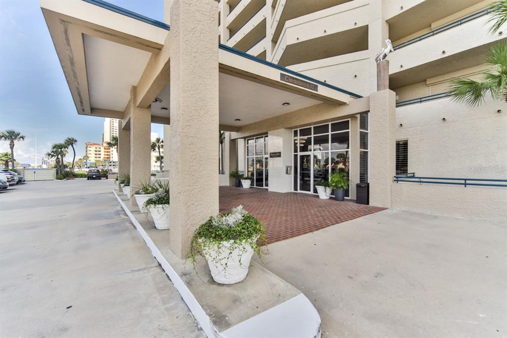 The exterior entrance of a multi-story building features a covered driveway and potted plants — 3425 S ATLANTIC AVENUE UNIT 1102, DAYTONA BEACH, FL