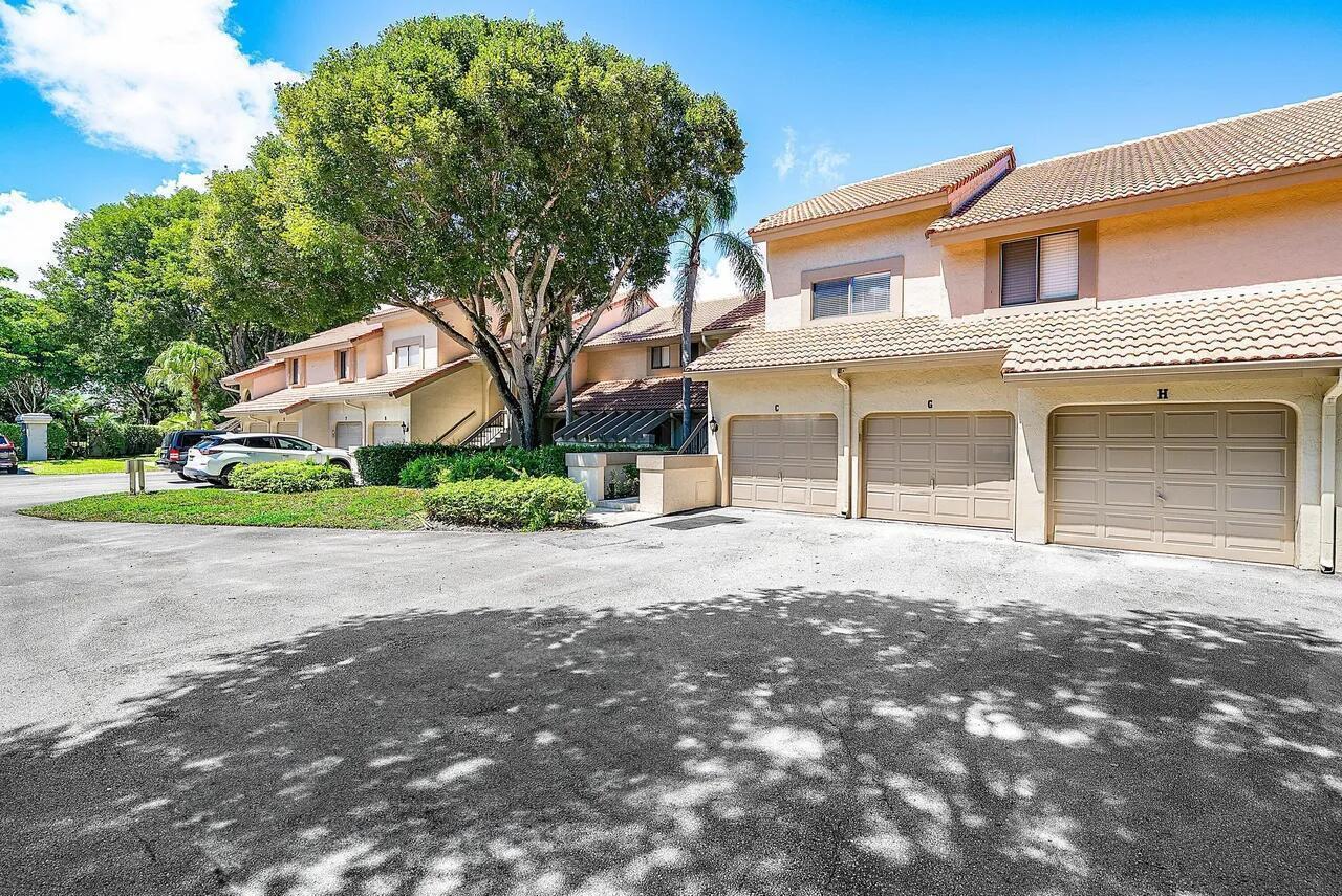 An exterior view of a multi-unit residential building with beige stucco walls and garage doors — 5520 Coach House Circle # G, Boca Raton FL 33486, BOCA RATON, FL