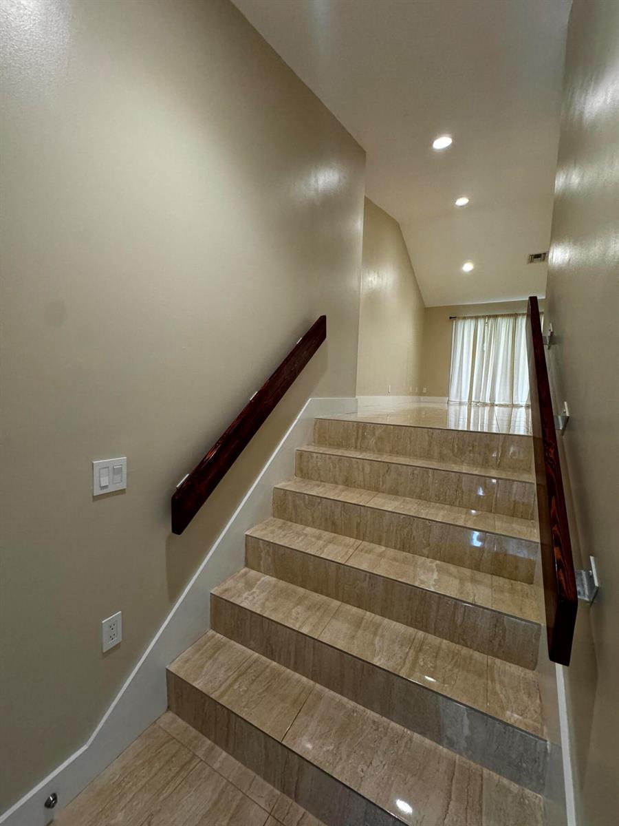 A staircase with beige tiled steps and dark wood handrails leads to an upper landing — 5520 Coach House Circle # G, Boca Raton FL 33486, BOCA RATON, FL