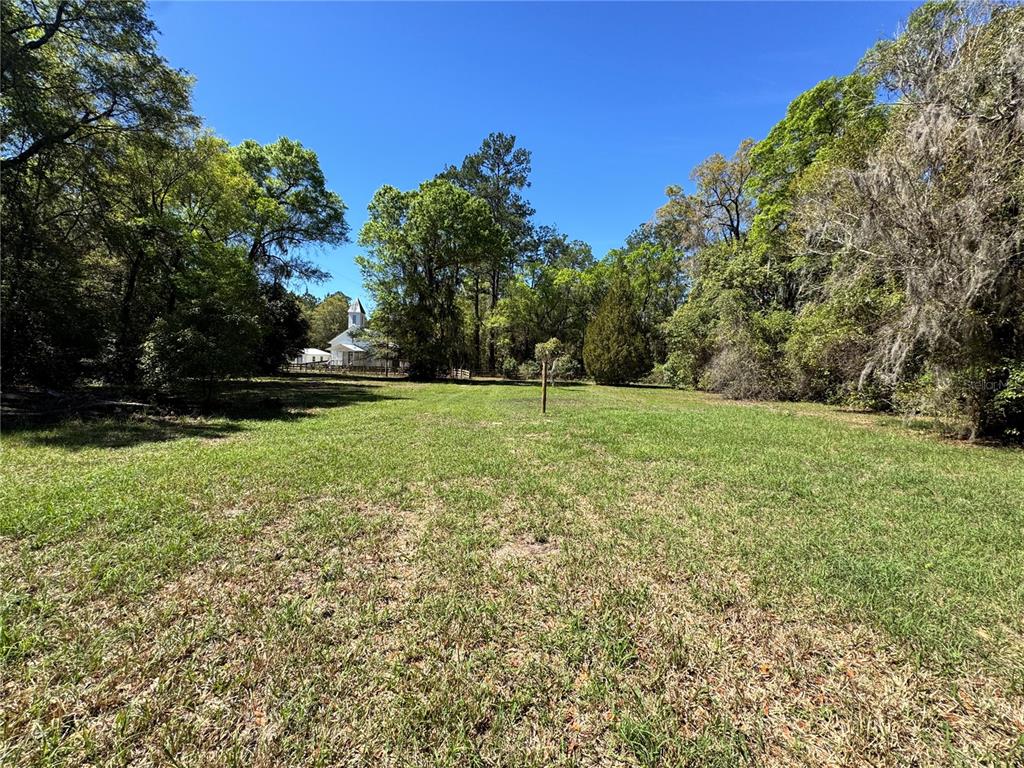 A grassy, open lot is surrounded by mature trees with a white building in distance — 1336 NE 191ST TERRACE, HAWTHORNE, FL