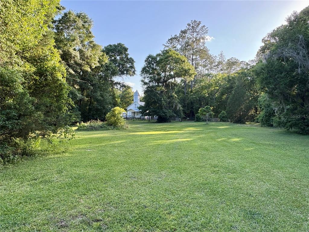A grassy field leads toward a white church building surrounded by dense trees — 1336 NE 191ST TERRACE, HAWTHORNE, FL
