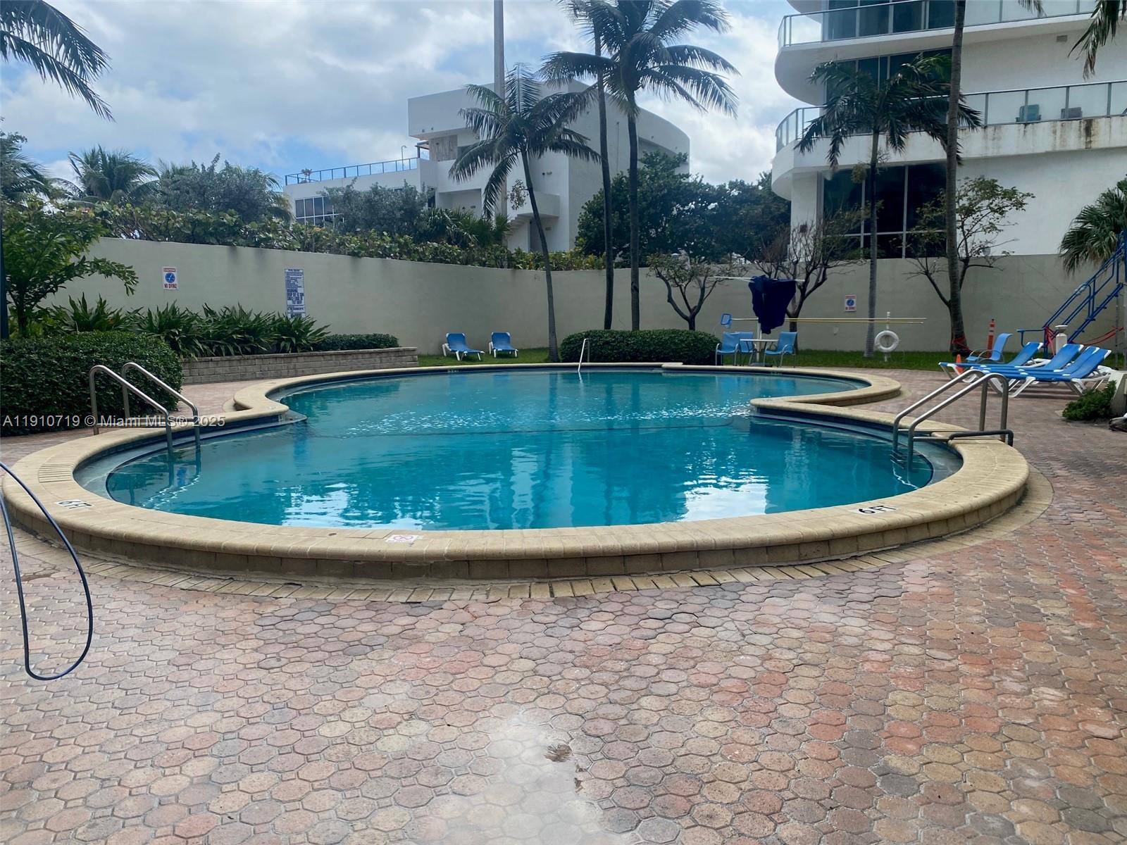 A kidney-shaped swimming pool sits on a paved patio surrounded by palm trees and buildings — 4001 S Ocean Dr # 14F, Hollywood FL 33019, HOLLYWOOD, FL