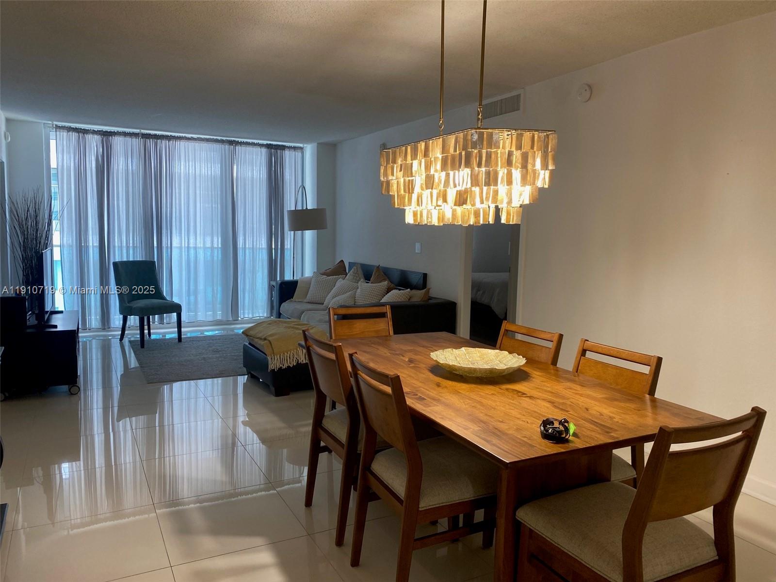 A dining area with a wooden table and chandelier opens into a living room — 4001 S Ocean Dr # 14F, Hollywood FL 33019, HOLLYWOOD, FL