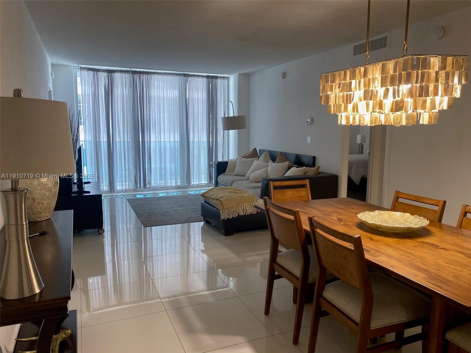 A living and dining area features tile floors, a wooden table, and a chandelier — 4001 S Ocean Dr # 14F, Hollywood FL 33019, HOLLYWOOD, FL