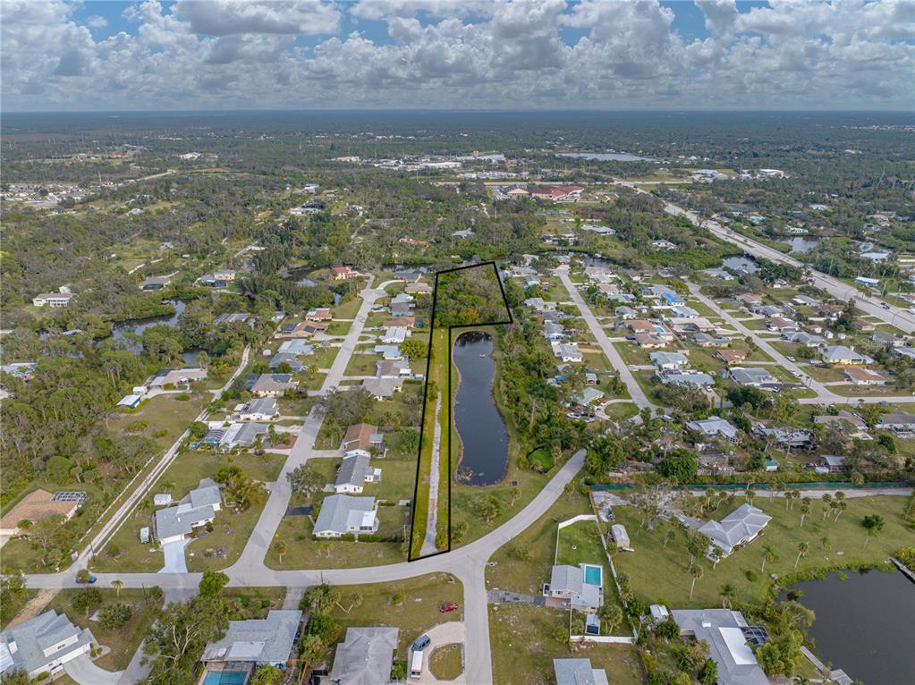 An aerial view shows a vacant, narrow, wooded lot adjacent to a pond in a neighborhood — STRATFORD 1B ROAD, ENGLEWOOD, FL
