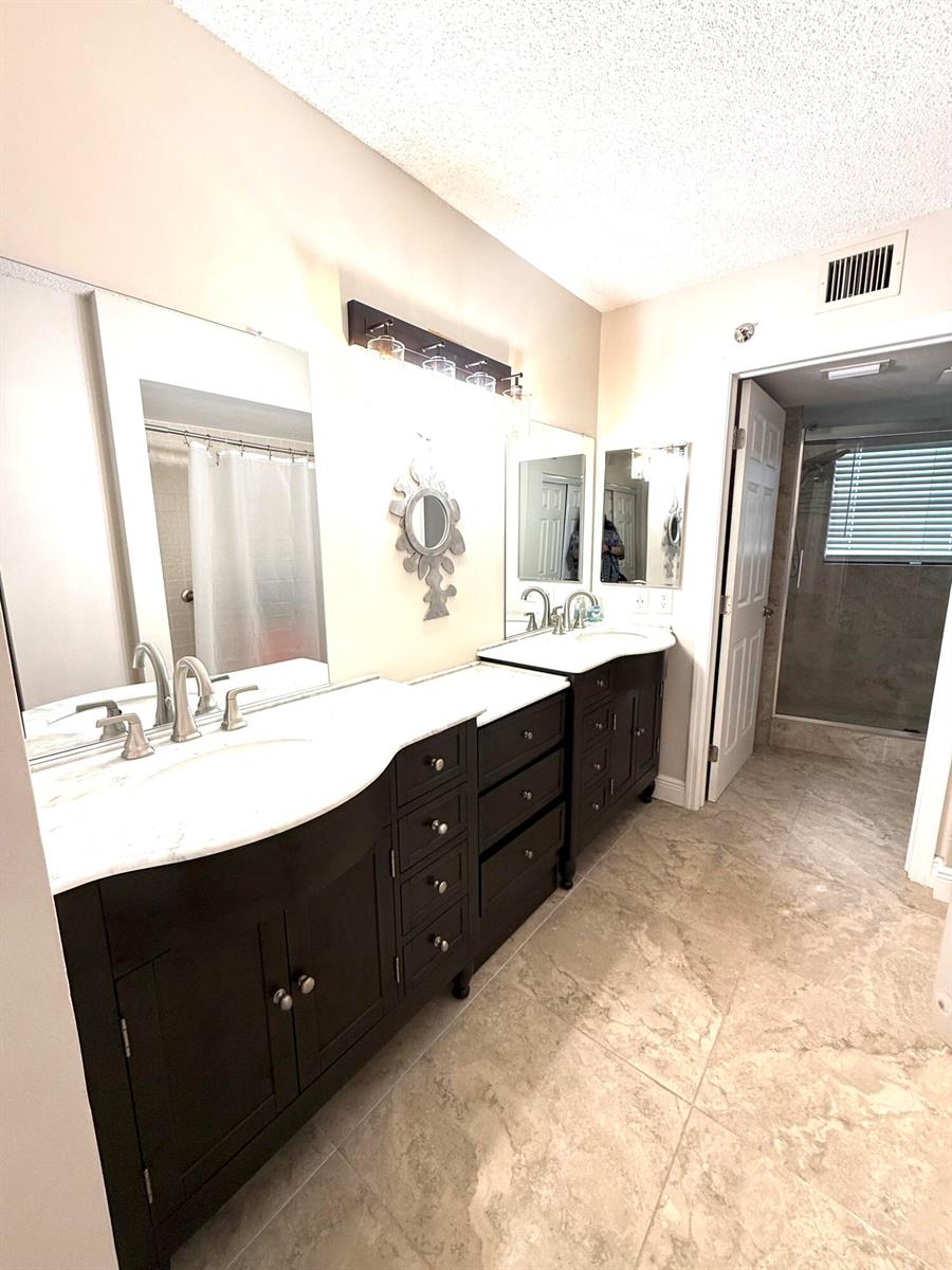 A bathroom features a double vanity with dark cabinets, white countertops, and a walk-in shower — 7380 S Oriole Boulevard # 606, Delray Beach FL 33446, DELRAY BEACH, FL