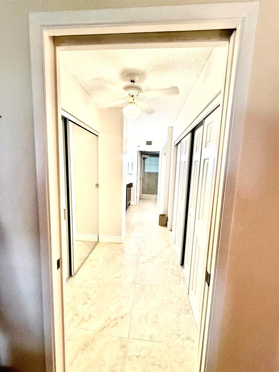 A hallway with tiled floors leads to a bathroom, flanked by mirrored and paneled closets — 7380 S Oriole Boulevard # 606, Delray Beach FL 33446, DELRAY BEACH, FL