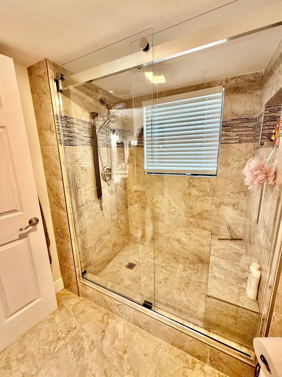 A walk-in shower with a glass door, built-in bench, and beige tile walls and flooring — 7380 S Oriole Boulevard # 606, Delray Beach FL 33446, DELRAY BEACH, FL