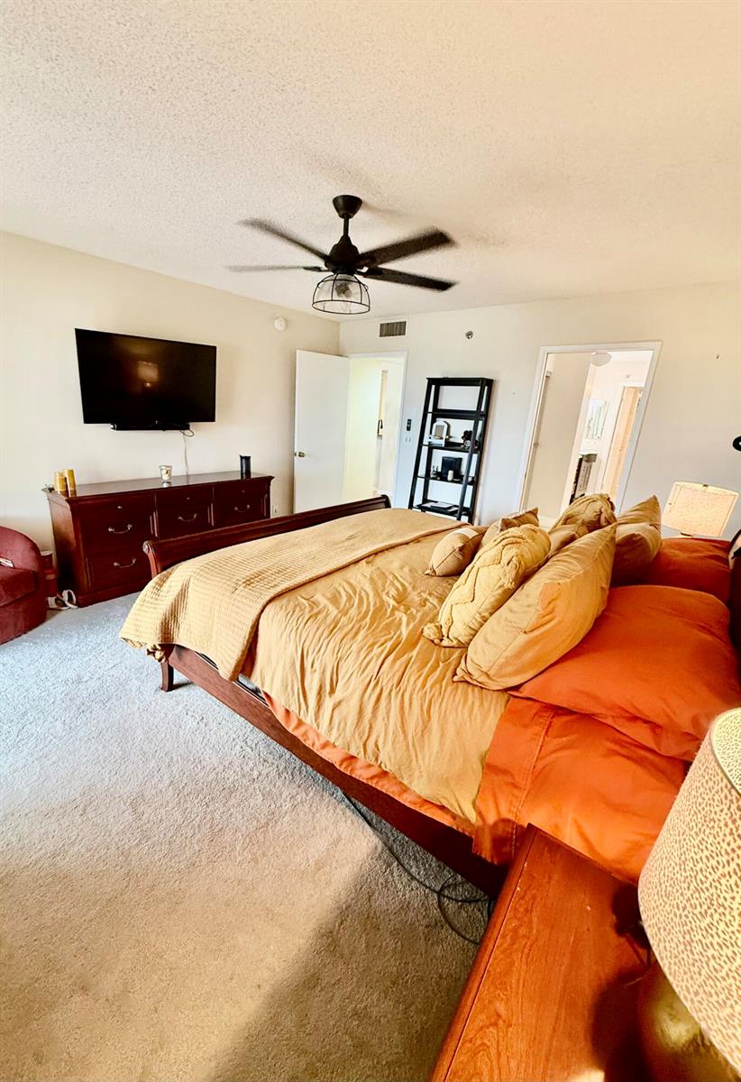 A bedroom features a large bed with orange bedding, a dark wood dresser, and a television — 7380 S Oriole Boulevard # 606, Delray Beach FL 33446, DELRAY BEACH, FL