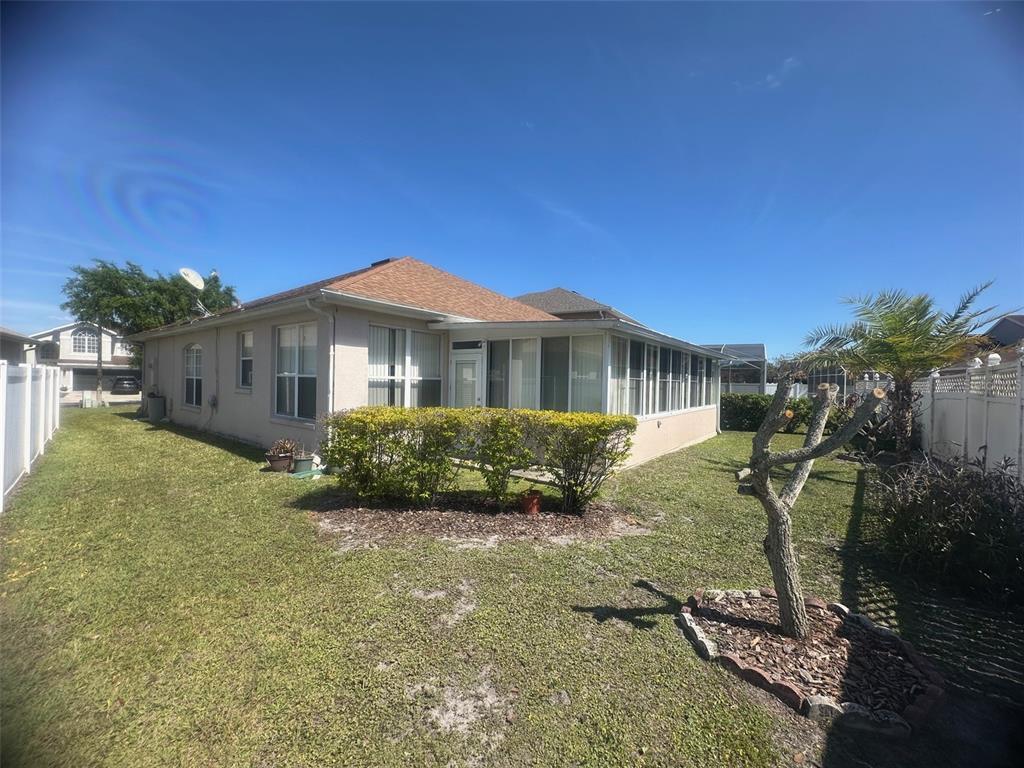 The exterior of a beige house features a sunroom, a grassy yard, and a tree — 14958 LAKE AZURE DRIVE, ORLANDO, FL