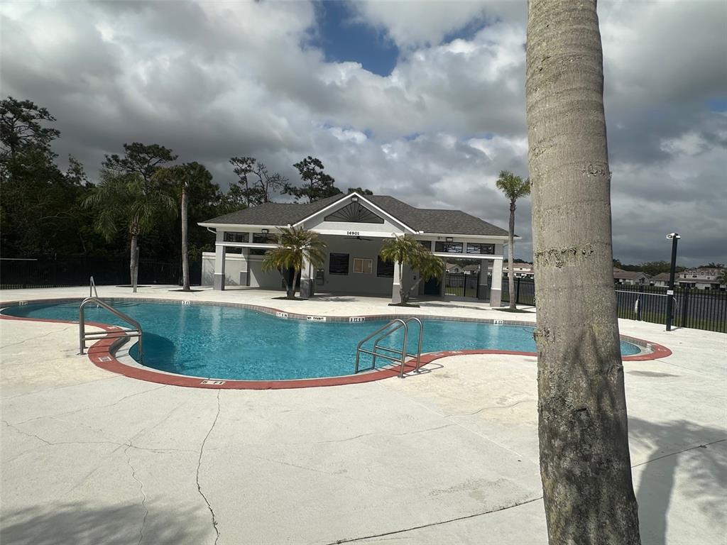 A swimming pool with a surrounding patio and a clubhouse building under a cloudy sky — 14958 LAKE AZURE DRIVE, ORLANDO, FL