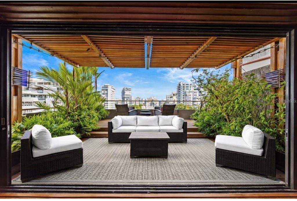A furnished outdoor terrace features a wooden pergola, lush greenery, and a city skyline view — 1223 LUCHETTI STREET UNIT 801, SAN JUAN, PR