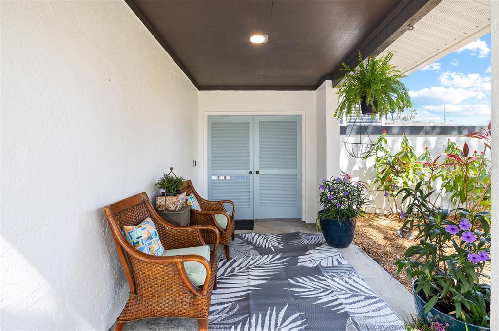 A covered patio features wicker chairs, a patterned rug, blue louvered doors, and potted plants — 15620 GARDENSIDE LANE, TAMPA, FL