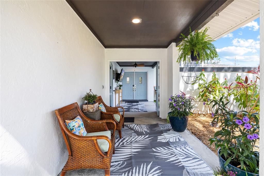 A covered patio features wicker chairs, a patterned rug, and potted plants near double doors — 15620 GARDENSIDE LANE, TAMPA, FL