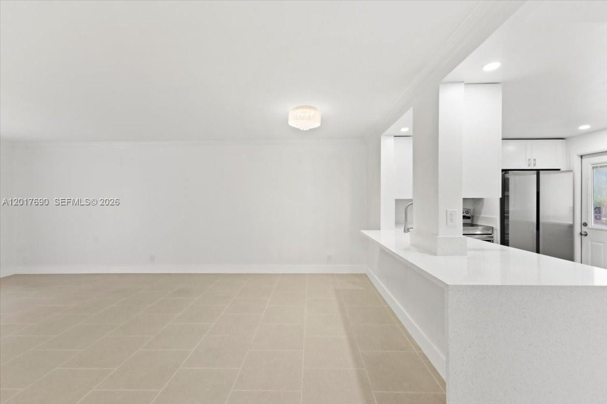 A bright, minimalist room features light tile flooring, white walls, and a kitchen breakfast bar — 319 NE 14TH AVE # 201, Hallandale Beach FL 33009, HALLANDALE BEACH, FL