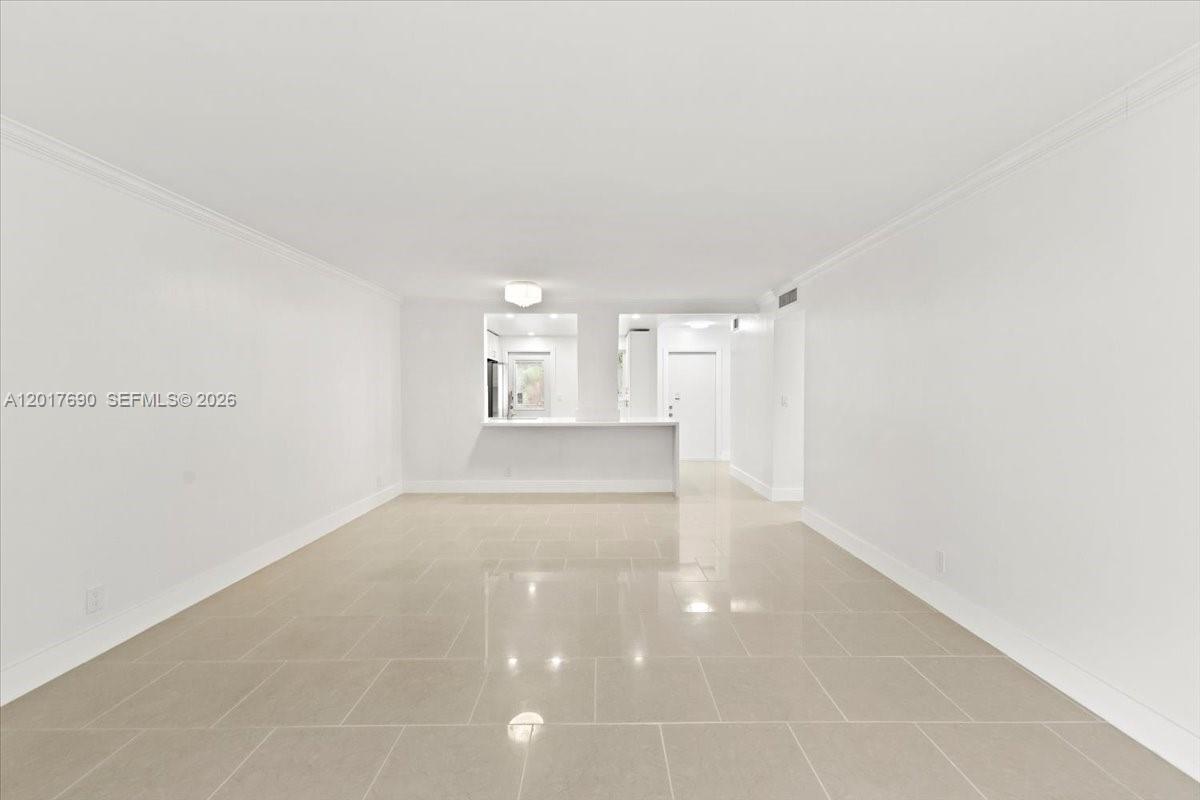 An empty room features light-colored tile flooring, white walls, and a pass-through kitchen counter — 319 NE 14TH AVE # 201, Hallandale Beach FL 33009, HALLANDALE BEACH, FL