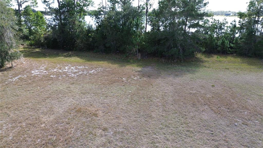 An elevated view of a grassy, vacant lot bordered by trees and a distant lake — 4094 CAMP SHORE DRIVE, SEBRING, FL