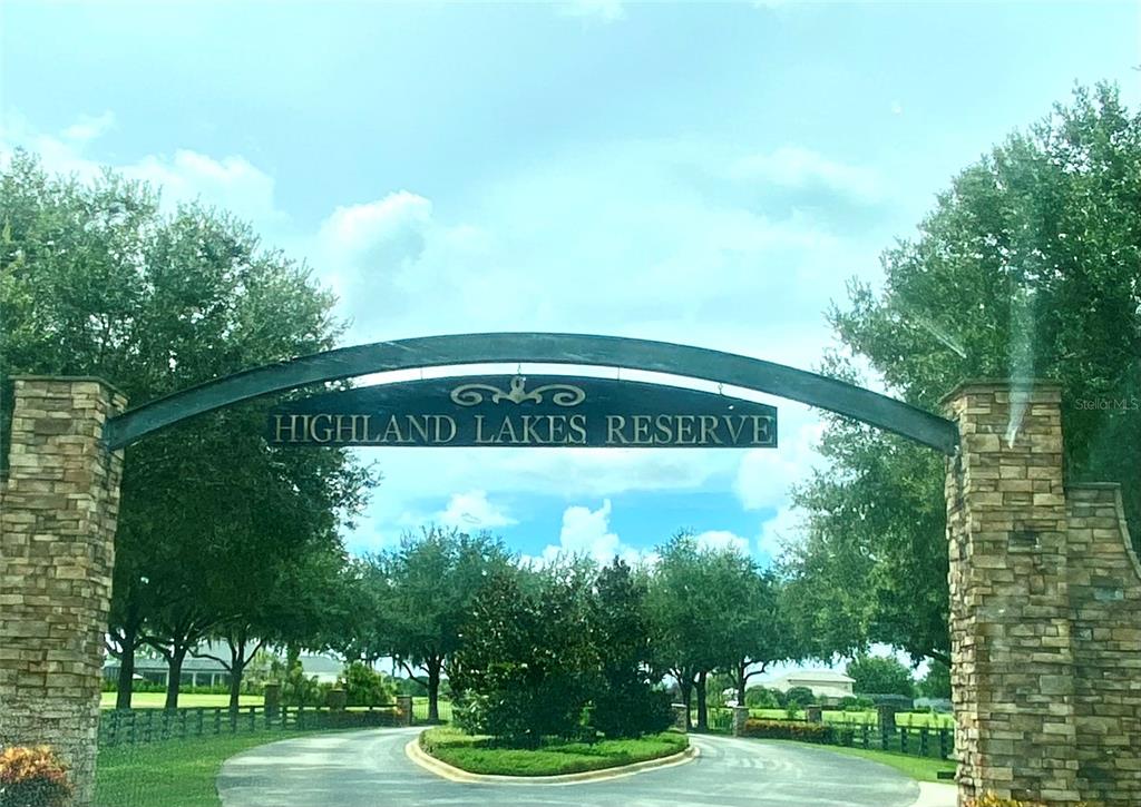A stone-pillared entrance archway with a sign reading Highland Lakes Reserve over a paved road — 4094 CAMP SHORE DRIVE, SEBRING, FL