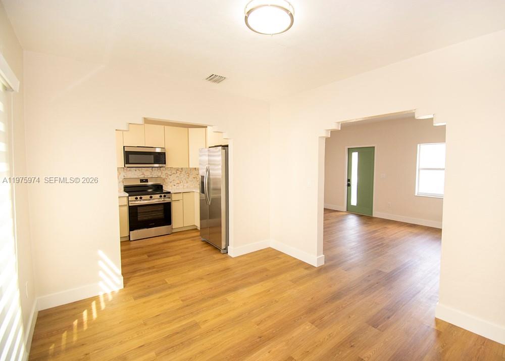 A kitchen with stainless steel appliances and wood-look flooring opens into an adjacent living area — 3200 SW 2nd St, Miami FL 33135, MIAMI, FL
