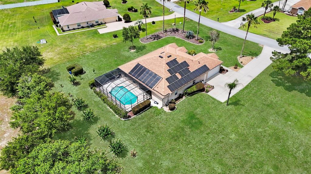 An aerial view of a suburban house with a pool enclosure and rooftop solar panels — 9908 SE 67TH AVENUE ROAD, BELLEVIEW, FL