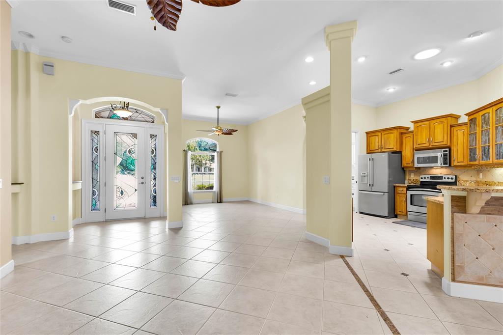 An open-concept living area with tile floors, yellow walls, and an adjacent kitchen with cabinets — 9908 SE 67TH AVENUE ROAD, BELLEVIEW, FL