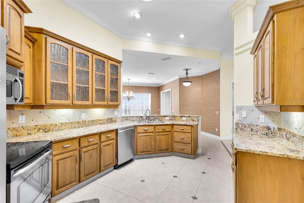 A kitchen with wood cabinets, granite countertops, stainless steel appliances, and light-colored tile flooring — 9908 SE 67TH AVENUE ROAD, BELLEVIEW, FL