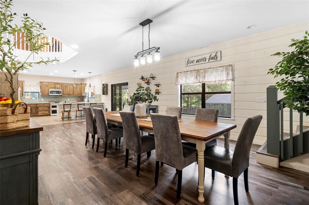 A dining room with a long wooden table, grey upholstered chairs, and a kitchen background — 1268 MCGREGOR ROAD, DELAND, FL