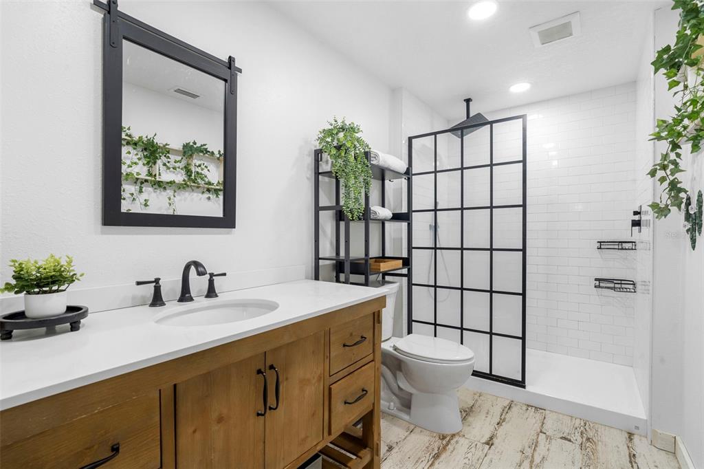 A bathroom features a wooden vanity, a walk-in shower with black grid doors, and greenery — 1268 MCGREGOR ROAD, DELAND, FL