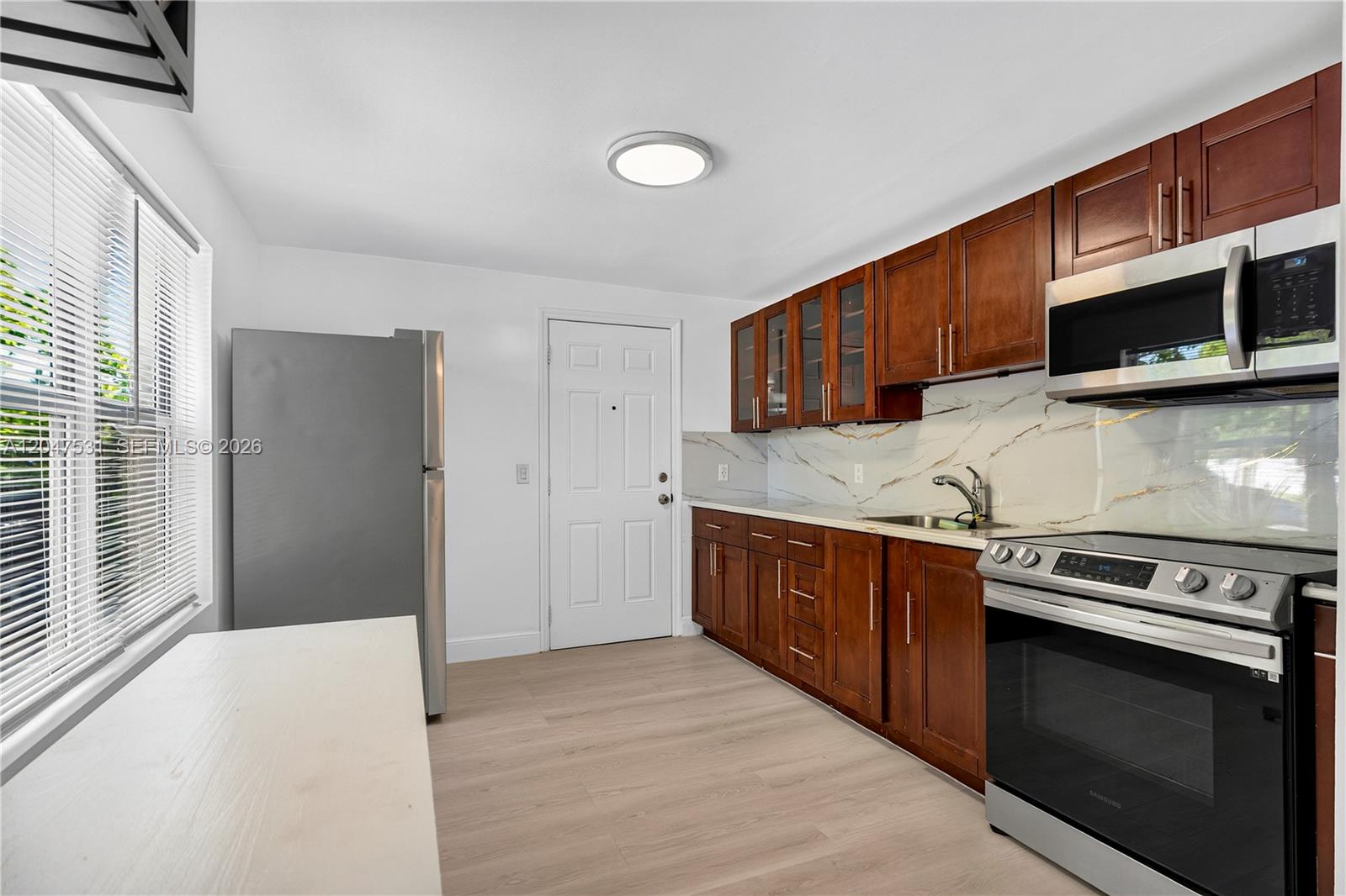 A kitchen features dark wood cabinets, stainless steel appliances, and a white marble-patterned backsplash — 5800 Taylor St # 1, Hollywood FL 33021, HOLLYWOOD, FL