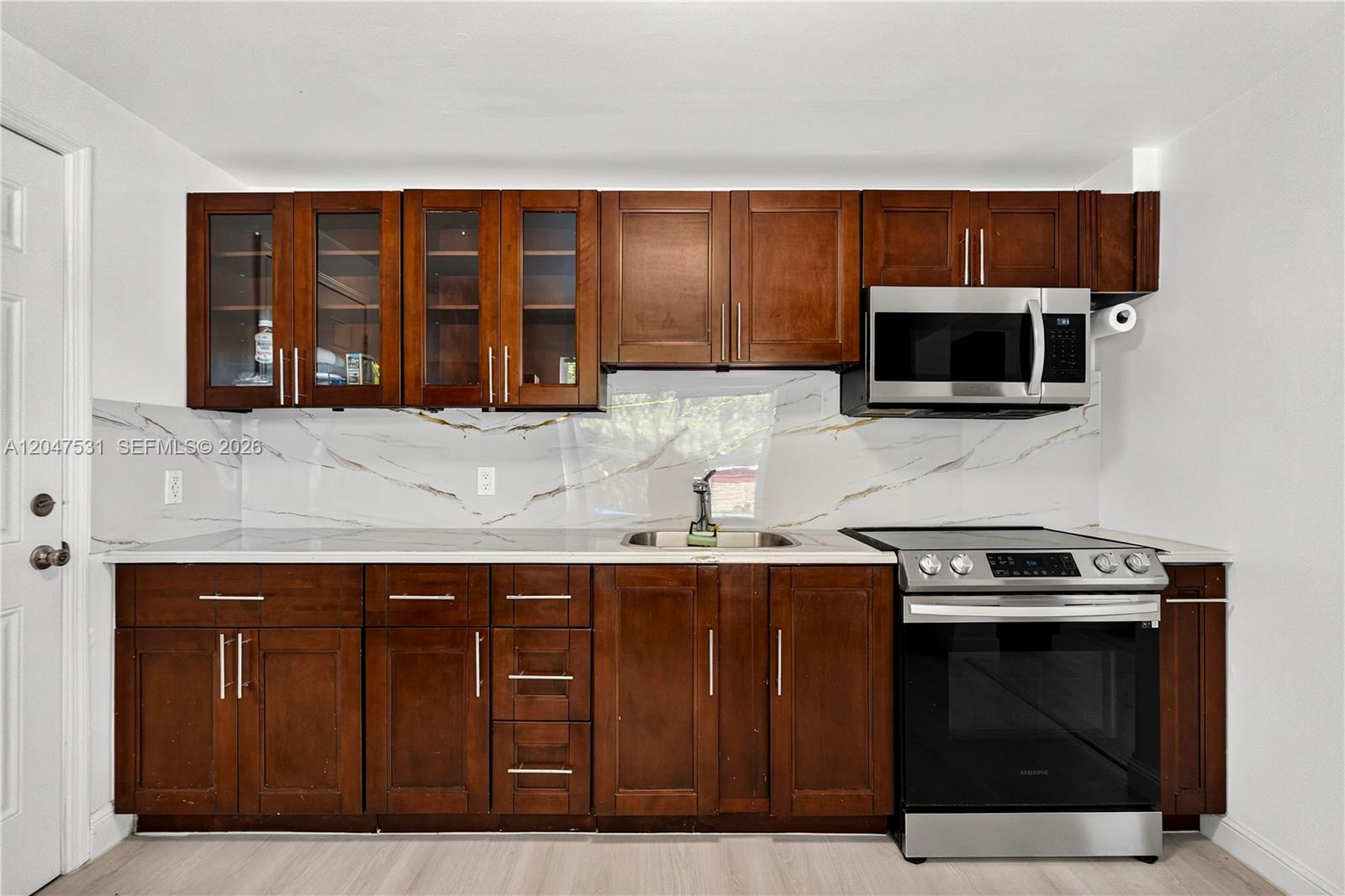 A kitchen features dark wood cabinets, stainless steel appliances, and a white marble-patterned backsplash — 5800 Taylor St # 1, Hollywood FL 33021, HOLLYWOOD, FL