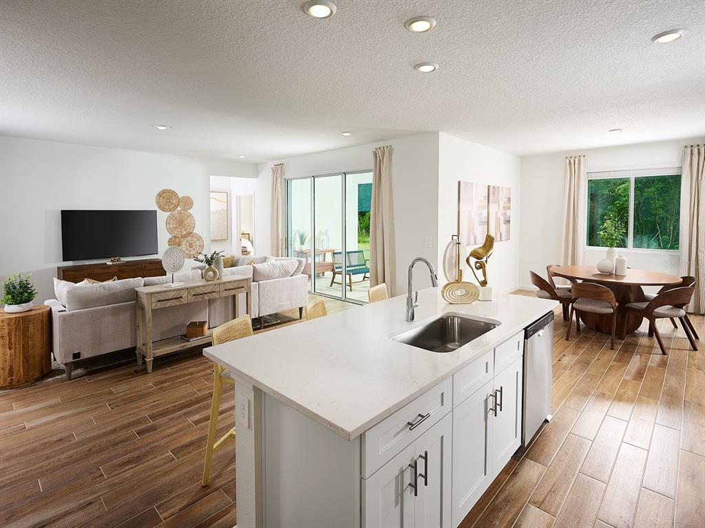 This open-concept kitchen features a white island, stainless steel sink, and wood-look tile flooring — 98 TEQUESTA COURT, PALM COAST, FL