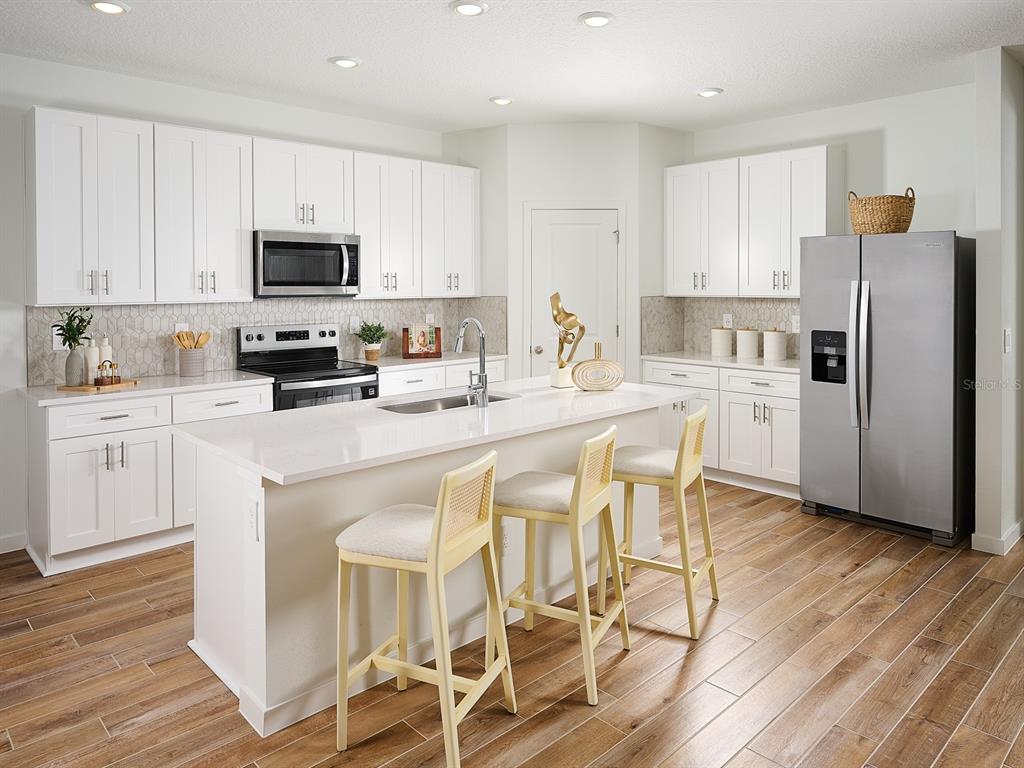 A modern kitchen features white cabinetry, a central island with bar stools, and stainless appliances — 98 TEQUESTA COURT, PALM COAST, FL