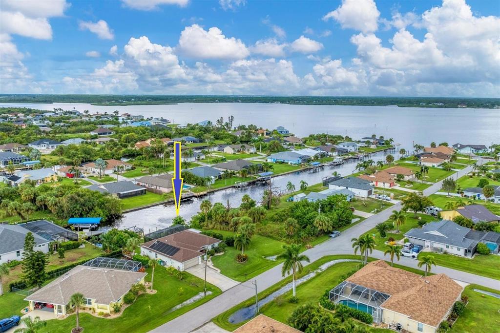 An aerial view shows a residential neighborhood with houses, a canal, and a large body of water — 2555 DIXON TERRACE, PORT CHARLOTTE, FL