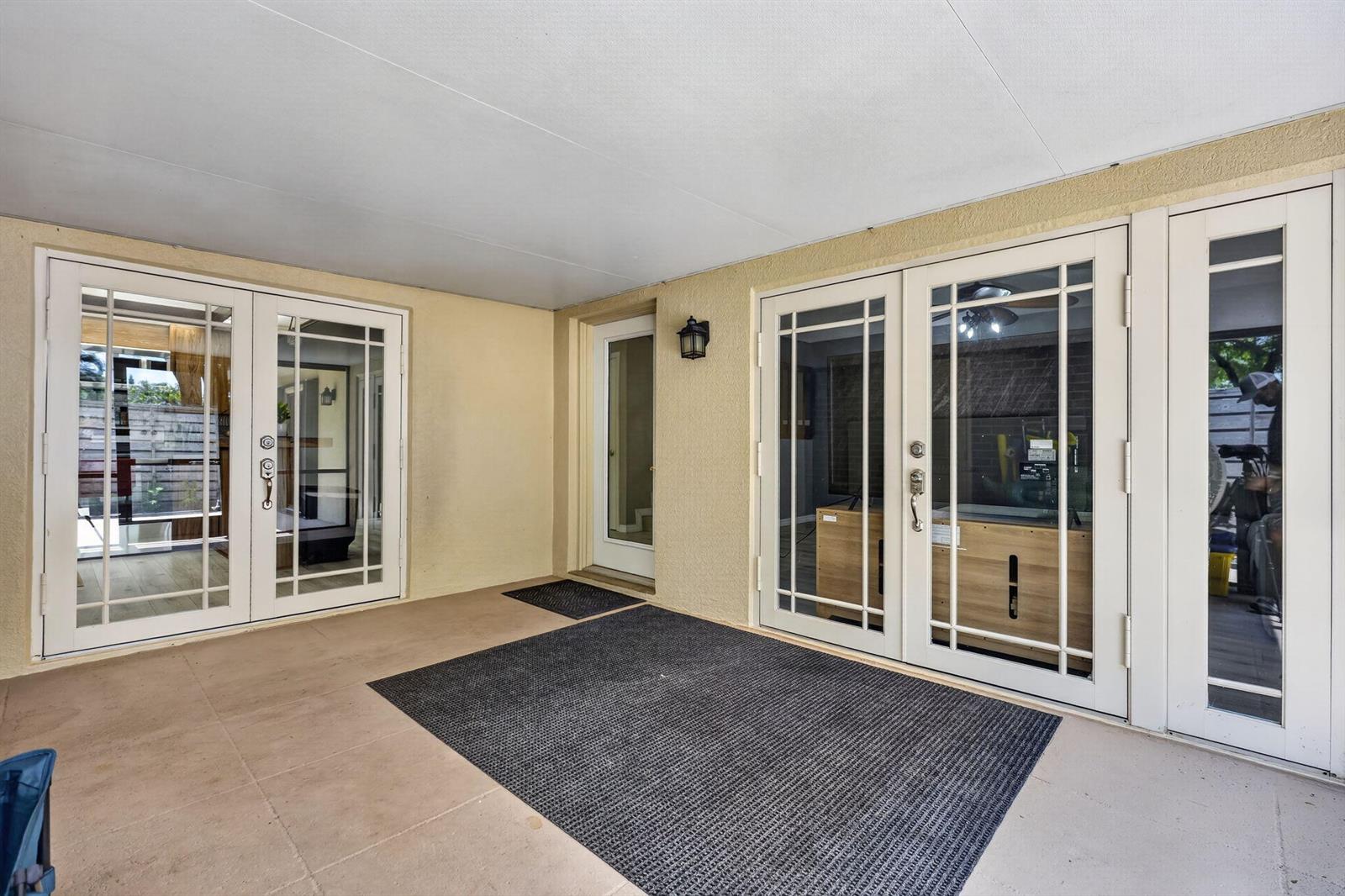 A covered patio features beige stucco walls, a concrete floor, and multiple glass-paneled doors — 527 5th Terrace, Palm Beach Gardens FL 33418, PALM BEACH GARDENS, FL