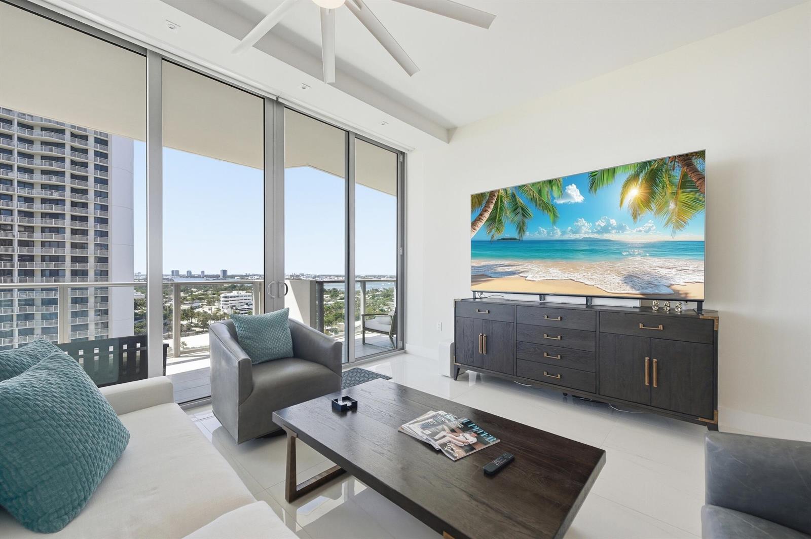 A modern living room features a large television, dark wood furniture, and a balcony view — 3100 N Ocean Drive # 1506, Singer Island FL 33404, SINGER ISLAND, FL