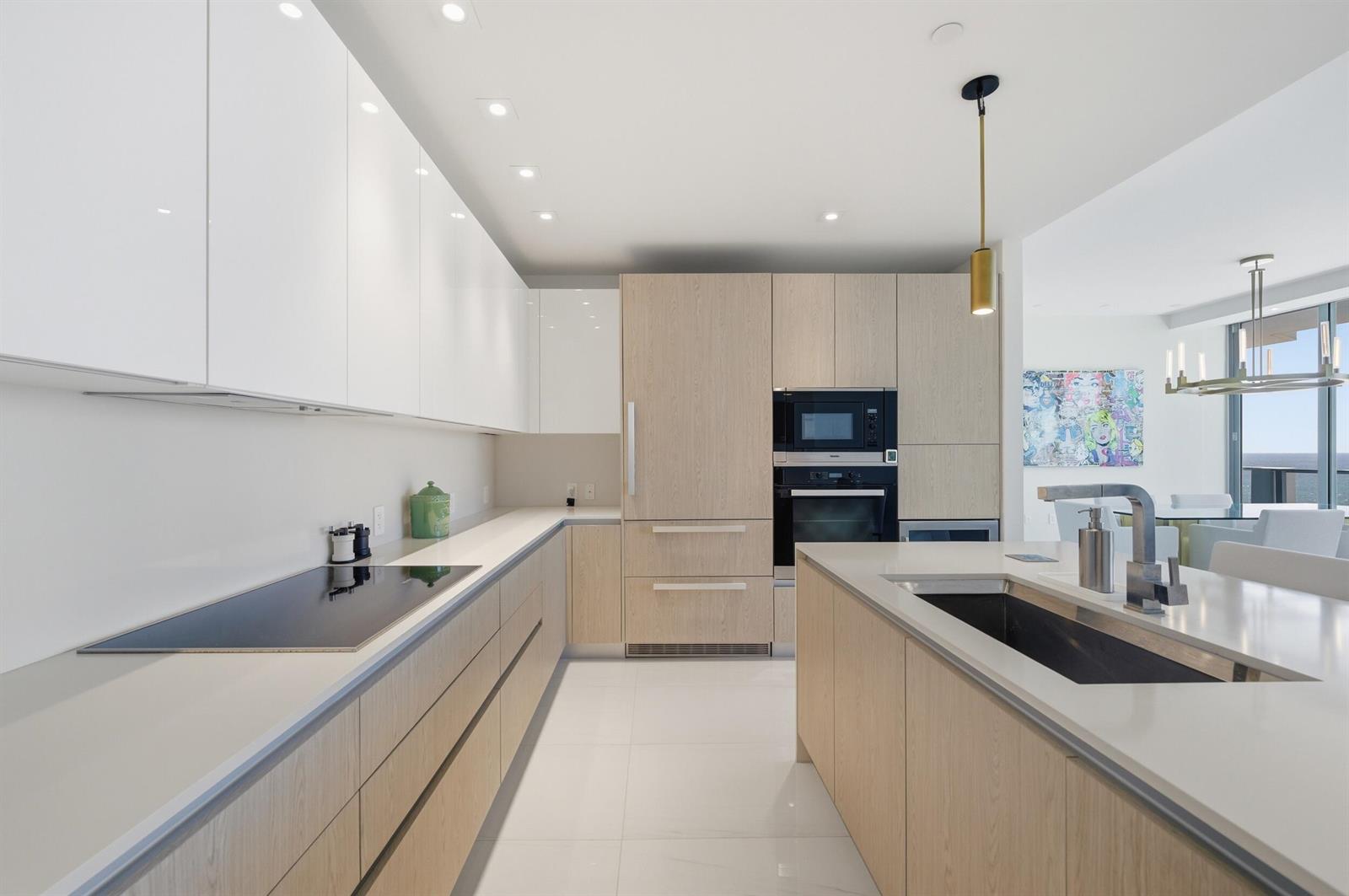 A modern kitchen features light wood cabinetry, white countertops, a central island, and integrated appliances — 3100 N Ocean Drive # 1506, Singer Island FL 33404, SINGER ISLAND, FL