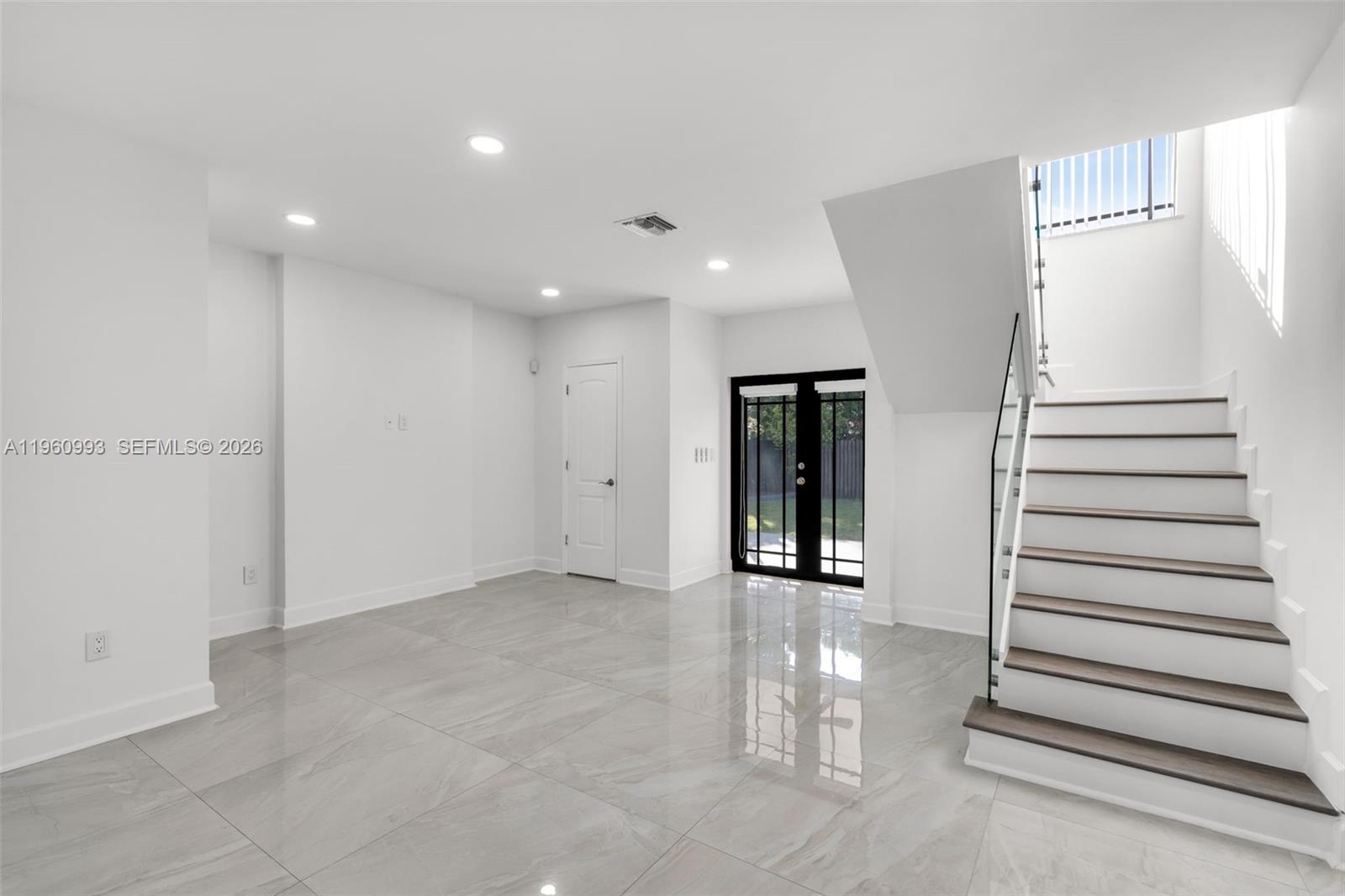 A minimalist room features white walls, large gray floor tiles, and a staircase with railings — 66 NW 73rd Place, Miami FL 33126, MIAMI, FL