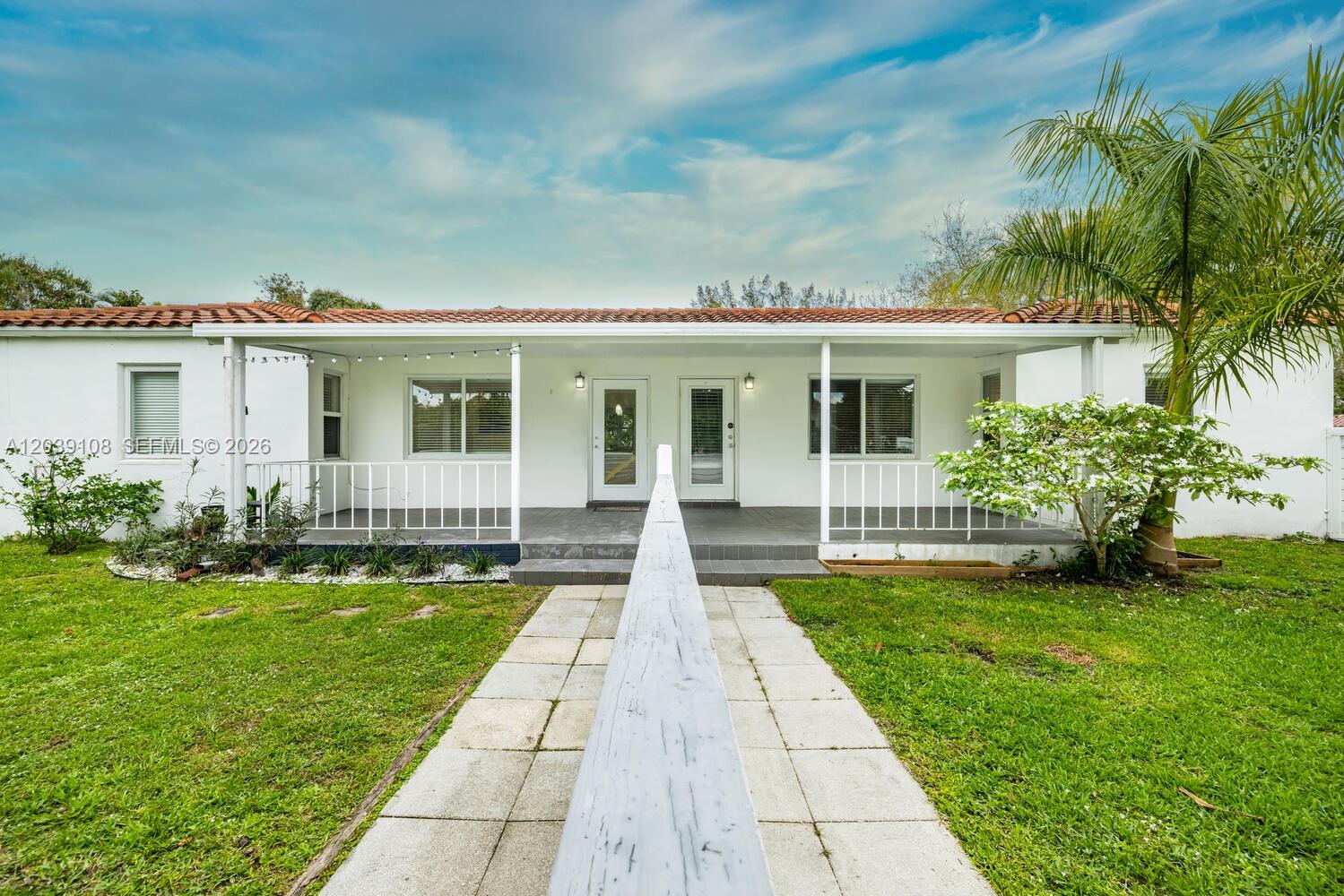 A single-story white house features a covered front porch, tiled roof, and a walkway — 1029 NE 113 St, Biscayne Park FL 33161, BISCAYNE PARK, FL