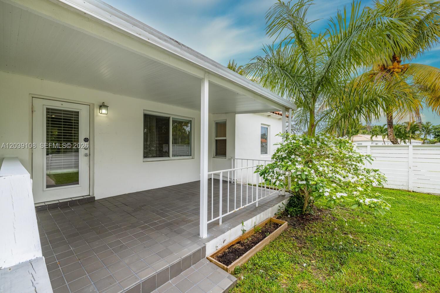A covered patio features gray tile flooring, a white railing, and a small garden bed — 1029 NE 113 St, Biscayne Park FL 33161, BISCAYNE PARK, FL