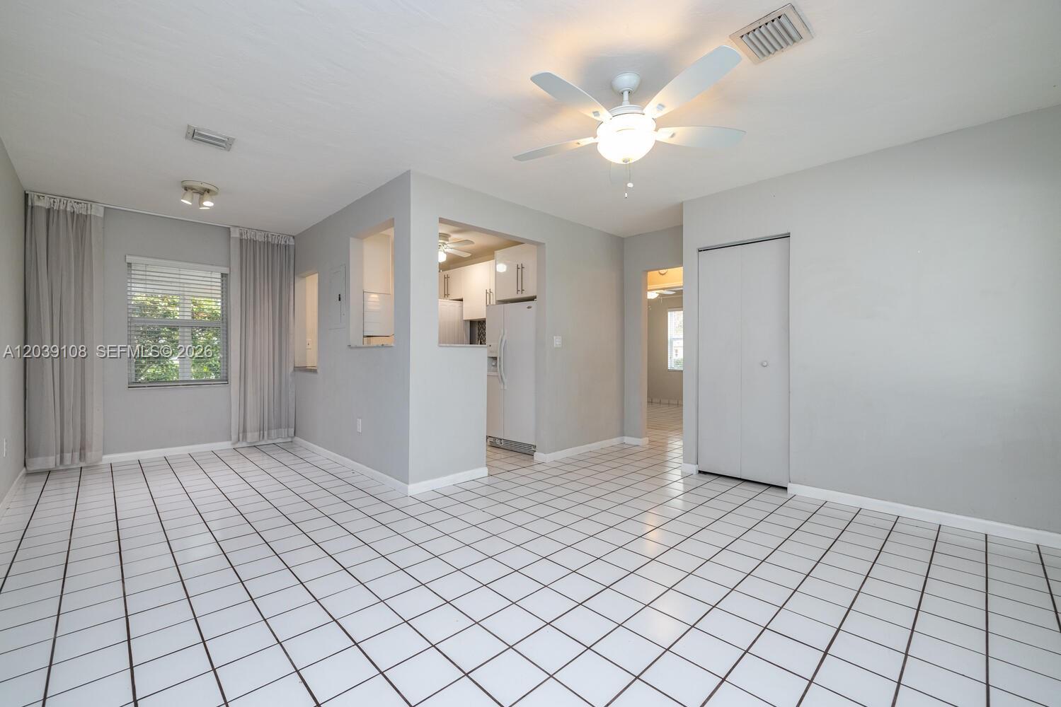 A living area with white tiled floors, a ceiling fan, and an adjacent kitchen — 1029 NE 113 St, Biscayne Park FL 33161, BISCAYNE PARK, FL
