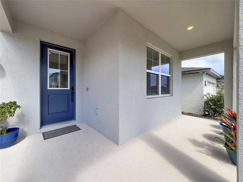 A covered entryway features a blue front door, a window, and light-colored concrete flooring — 2271 BEAR PEAK ROAD, MINNEOLA, FL