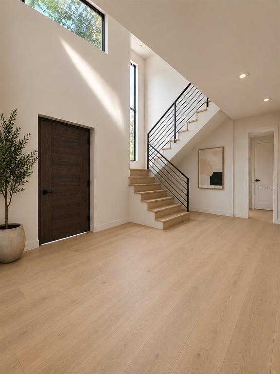 A bright entryway features light wood floors, a dark wood door, and a modern staircase — 5020 W HOMER AVENUE, TAMPA, FL
