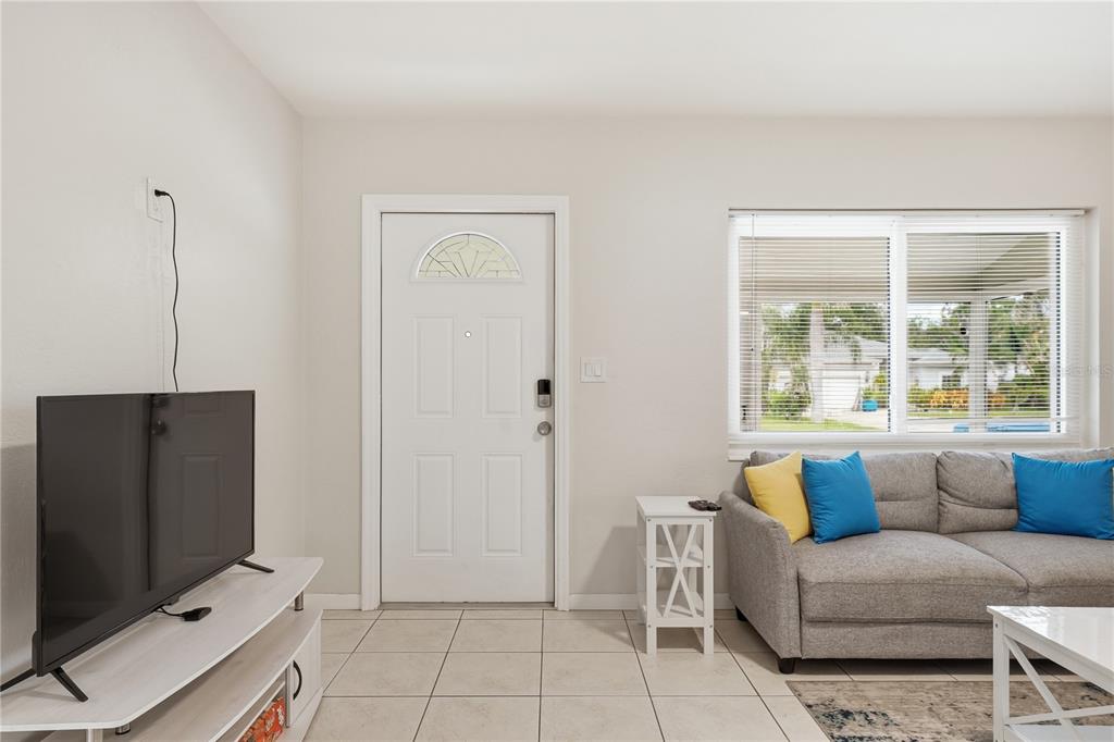 A living room features a white front door, a grey sofa, and a television console — 14512 117TH AVENUE, LARGO, FL