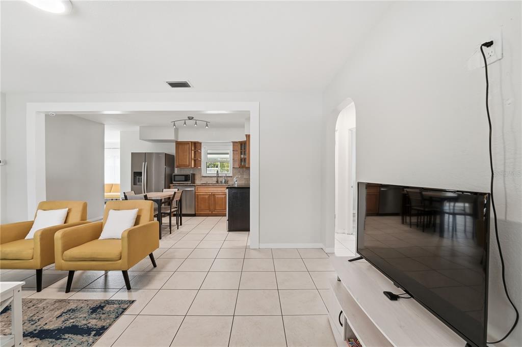 A living room with yellow armchairs and tile flooring opens into a kitchen with cabinets — 14512 117TH AVENUE, LARGO, FL