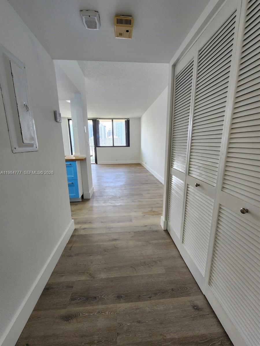 A hallway with wood-look flooring leads to a kitchen and a living area with windows — 520 Brickell Key Dr # A1517, Miami FL 33131, MIAMI, FL
